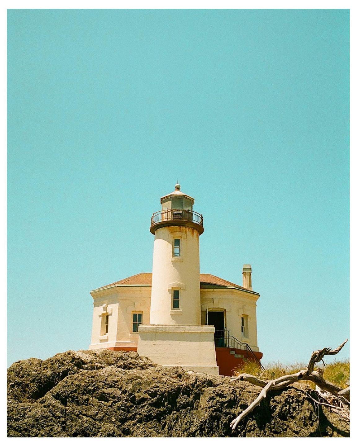 A lighthouse stands on a rocky cliff under a clear blue sky.