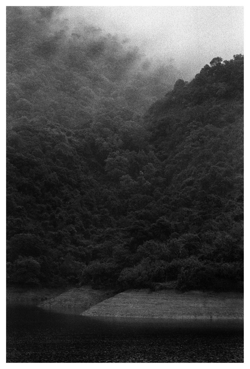 A body of water sits at the base of a large, tree-covered mountain shrouded in mist.