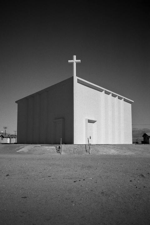 A modern church with a cross on its roof stands in a barren landscape under a clear sky.