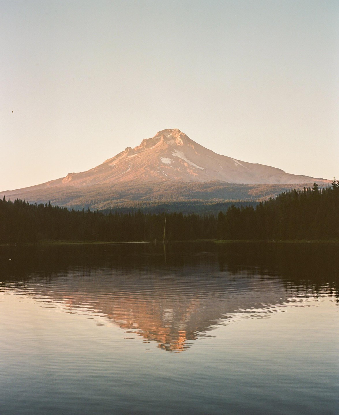 A mountain with a snow-capped peak is reflected in a calm lake surrounded by a forest.