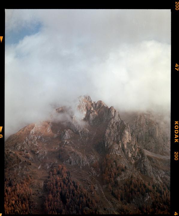 Clouds partially obscure the peaks of a mountain range covered in autumn foliage.