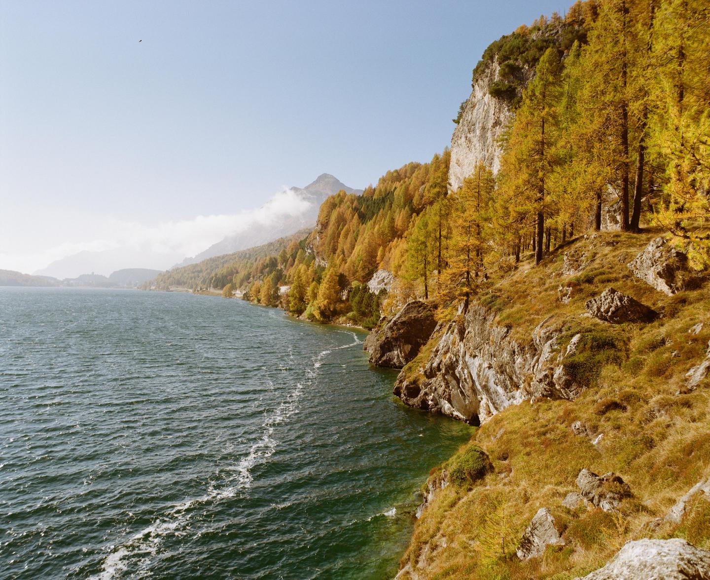 A body of water is next to a rocky, tree-covered mountain under a clear sky.