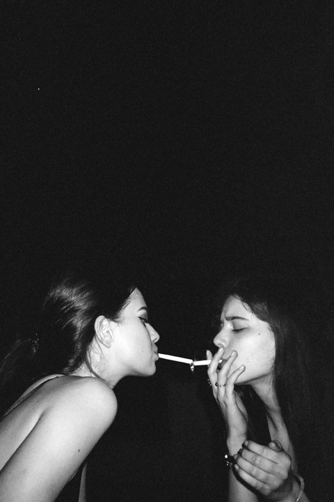 Two women are sharing a cigarette in the dark.