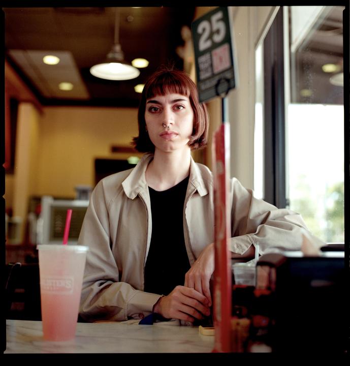 A woman with a nose ring sits at a table with a drink.