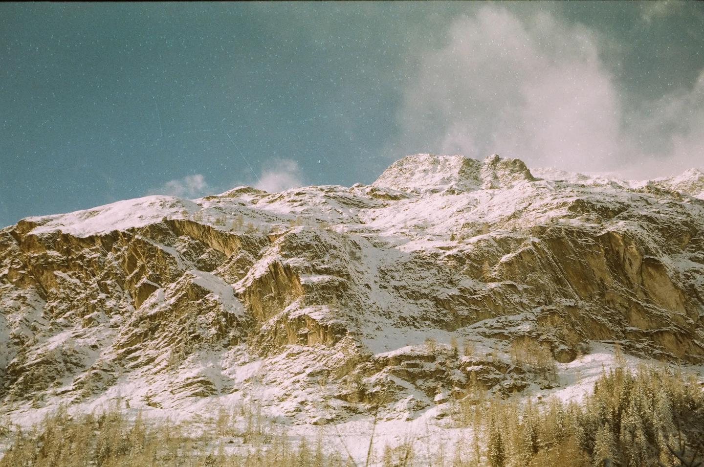 A snow-covered mountain rises under a blue sky with some clouds.