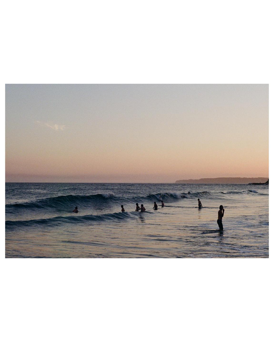 A group of people are swimming in the ocean at sunset.