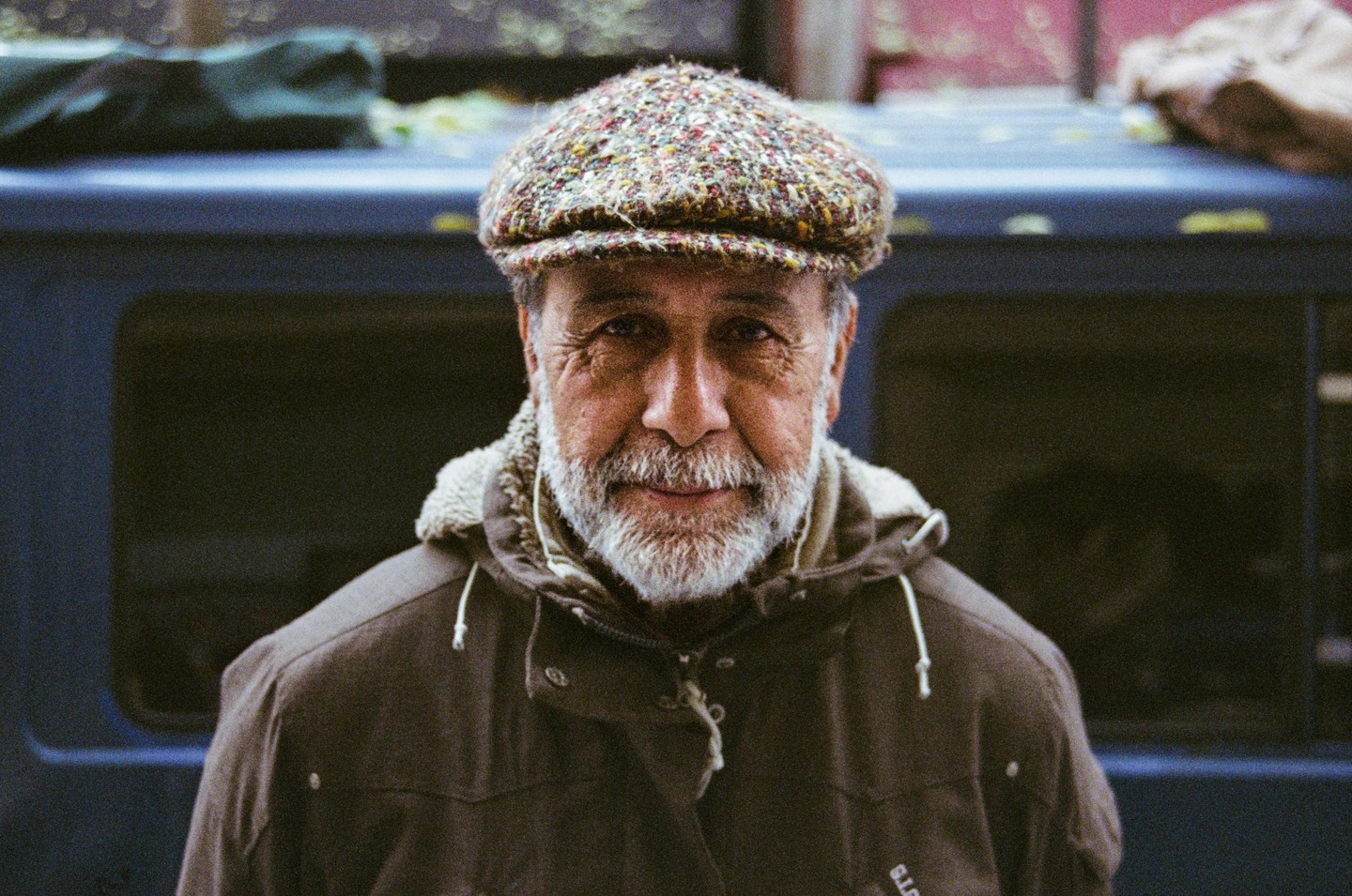 A man with a beard and a tweed cap looks directly at the viewer.