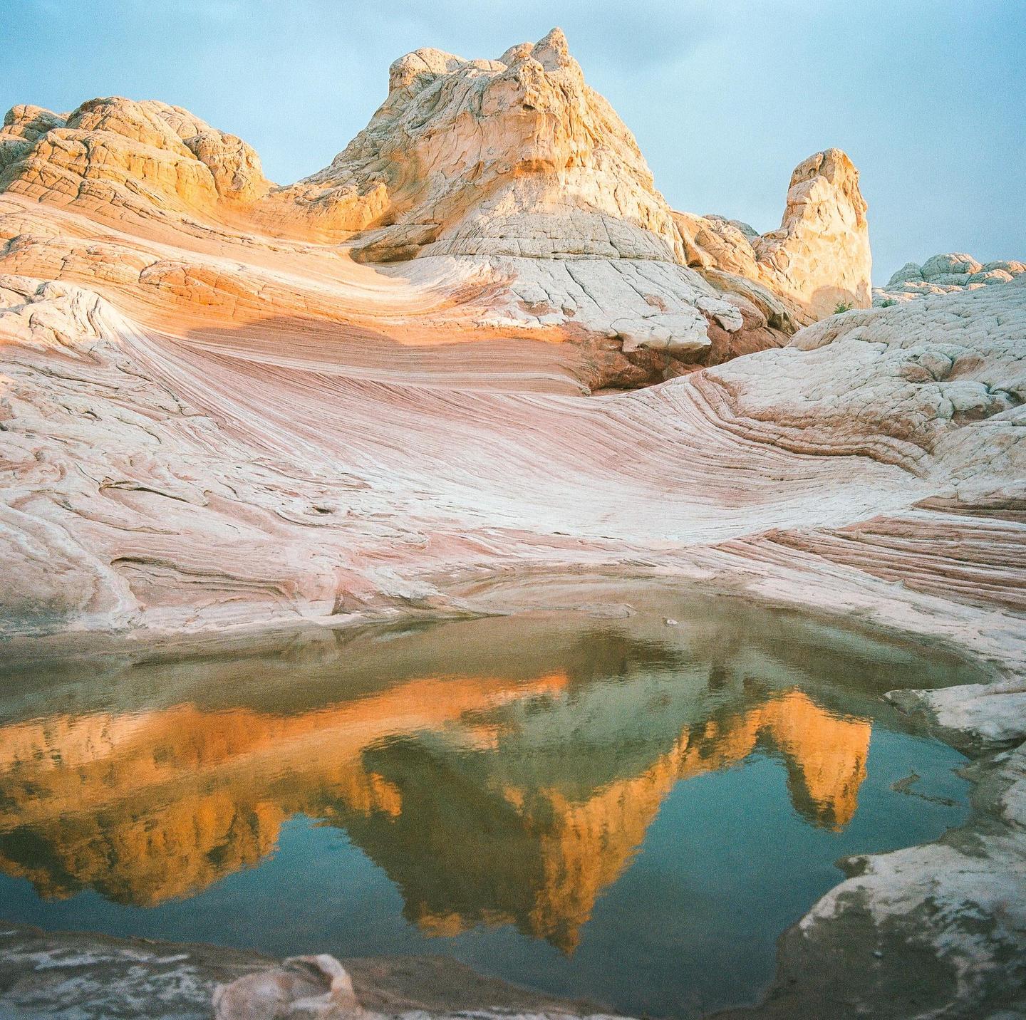 A small pool of water reflects a large rock formation under a blue sky.