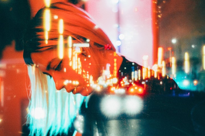 A woman with blonde hair is shown in profile with a double exposure of city lights.