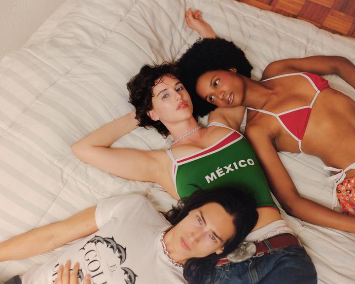 Three people are lying on a bed, looking up at the viewer.