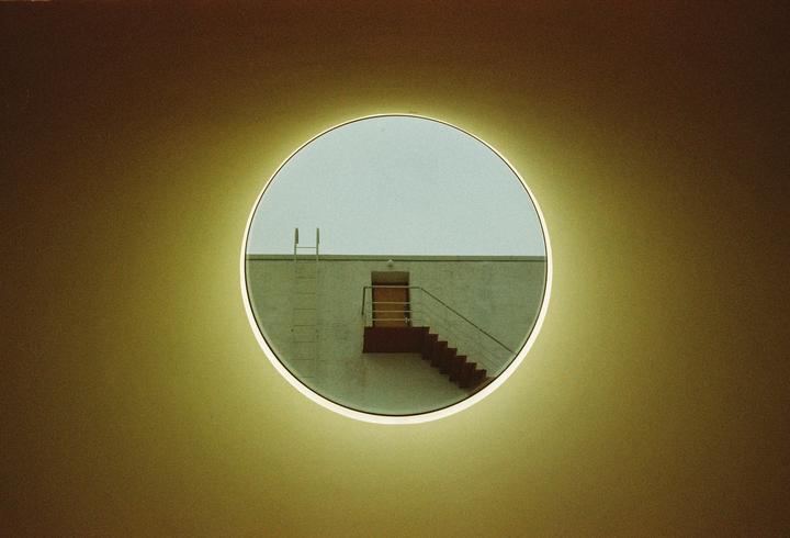 A circular window frames a building with an exterior staircase and a ladder leading to the roof.
