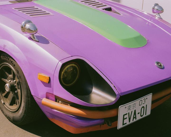 A purple car with a green stripe on the hood and a yellow headlight is parked on a sunny day.