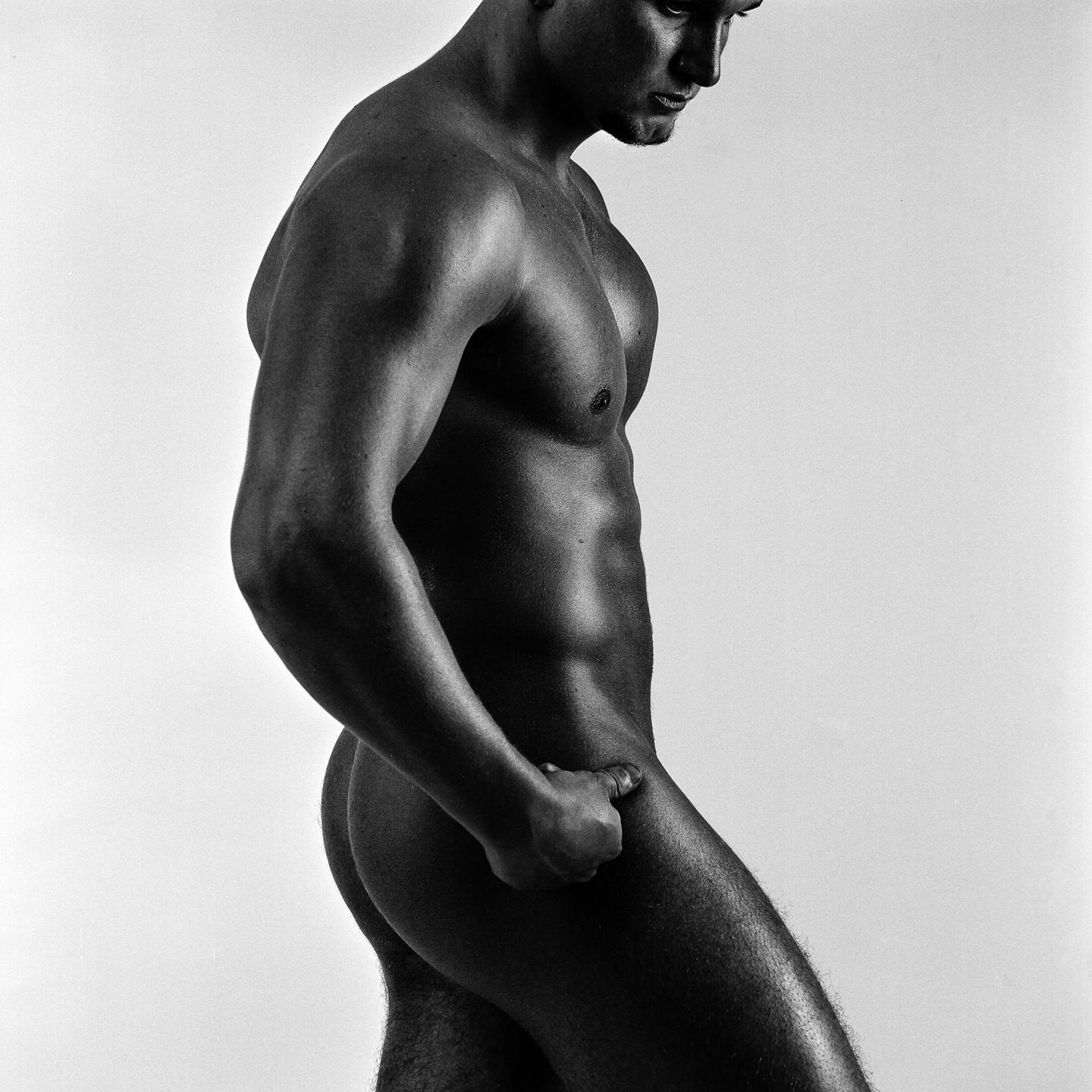 A man stands in profile with his head tilted down and his hand resting on his hip.