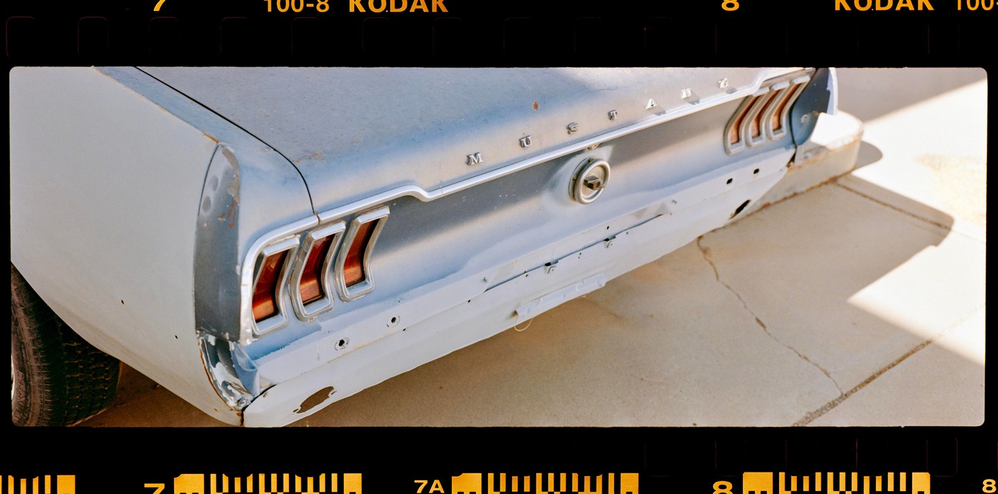 The rear of a light blue Ford Mustang is visible, with its taillights and trunk emblem.