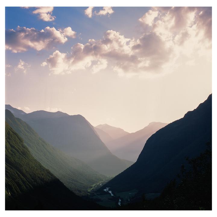 Sunlight streams through clouds into a valley with a river and mountains.