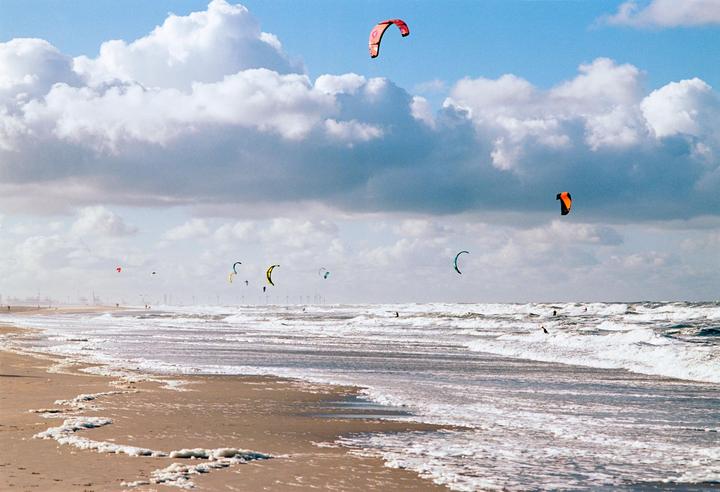Kitesurfers are visible in the North Sea with large clouds in the sky.
