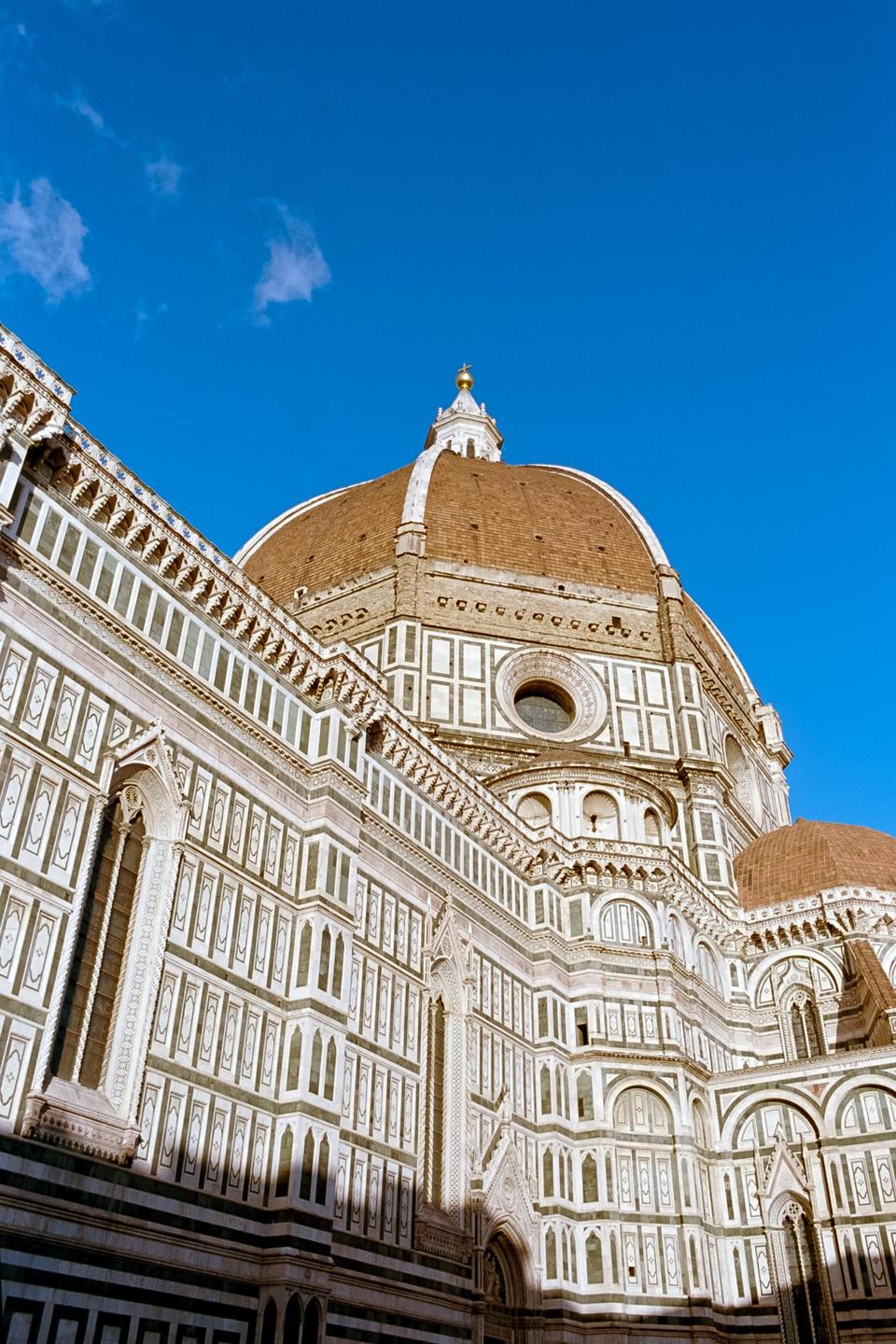 The dome of a large cathedral with intricate white and green patterns on its walls is visible against a clear blue sky.