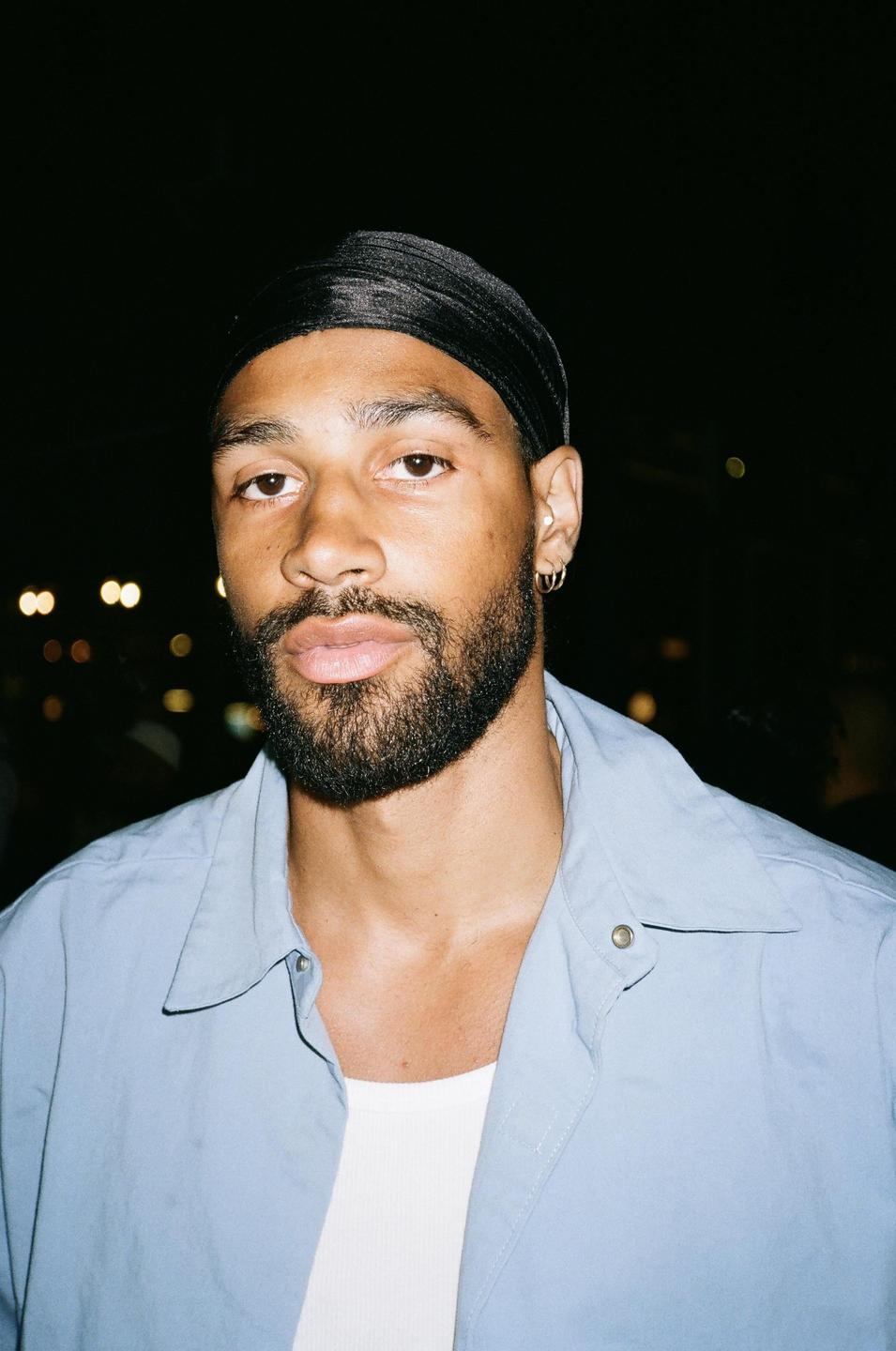 A man with a beard and a black durag looks directly at the viewer.