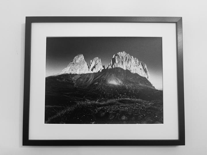 A framed black and white photograph of a mountain range with a dark shadow cast over the lower slopes is displayed on a white wall.