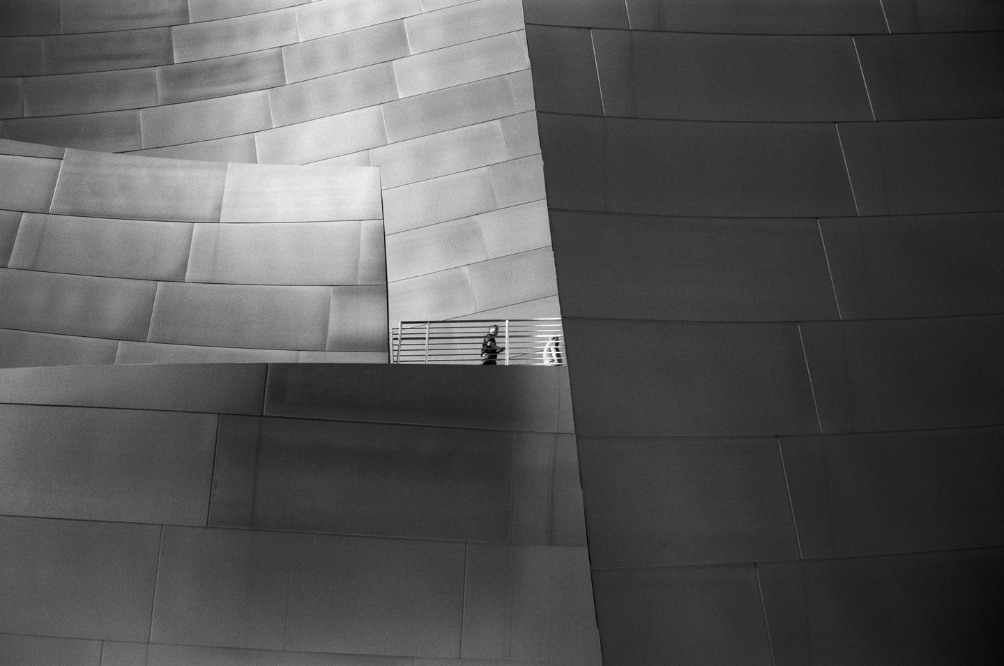 A person stands on a balcony of a building with a curved, paneled facade.