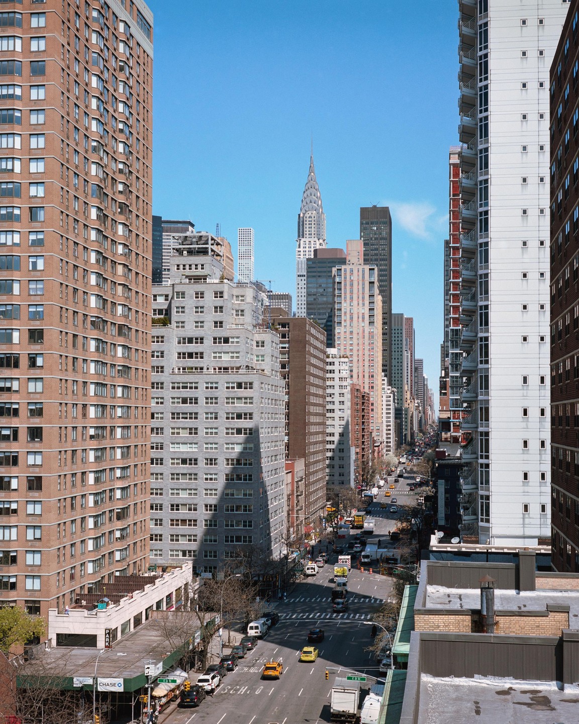 A street in New York City is visible between tall buildings with the Chrysler Building in the distance.