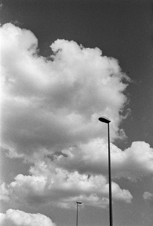 Two streetlights stand against a cloudy sky.