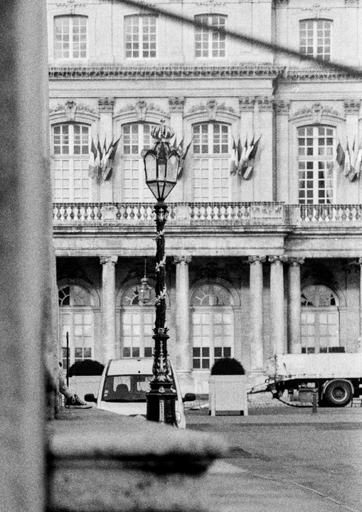 A street lamp stands in front of a classical building with flags hanging from its windows.