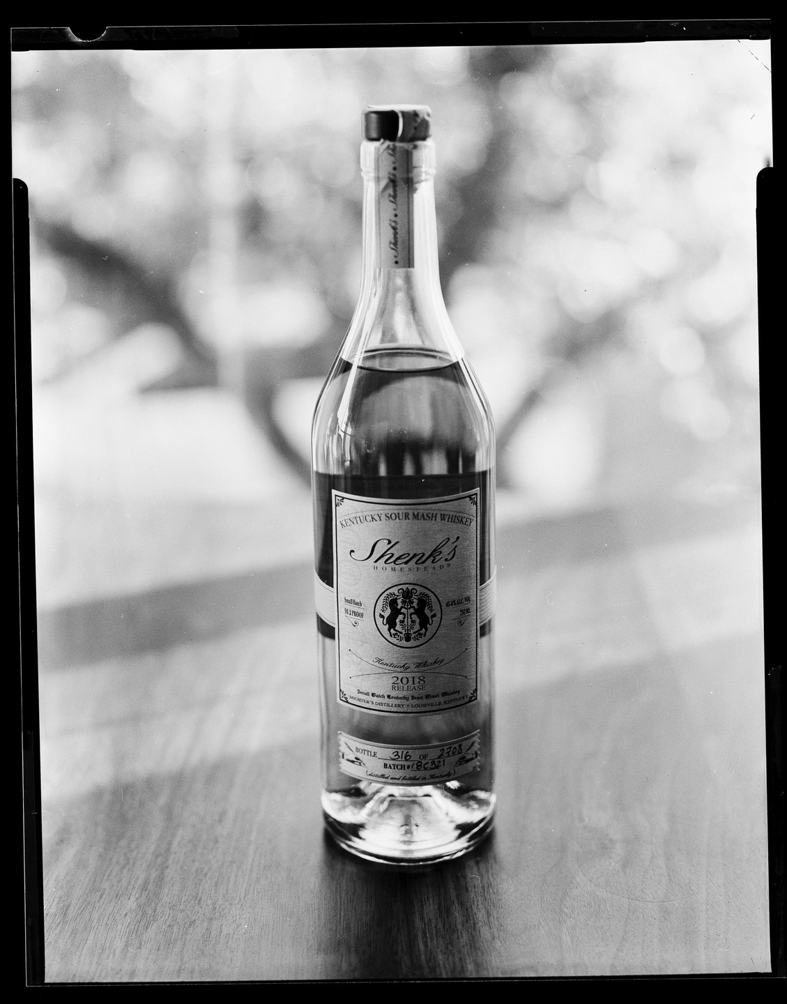 A bottle of Shenk's Kentucky Sour Mash Whiskey sits on a wooden surface.