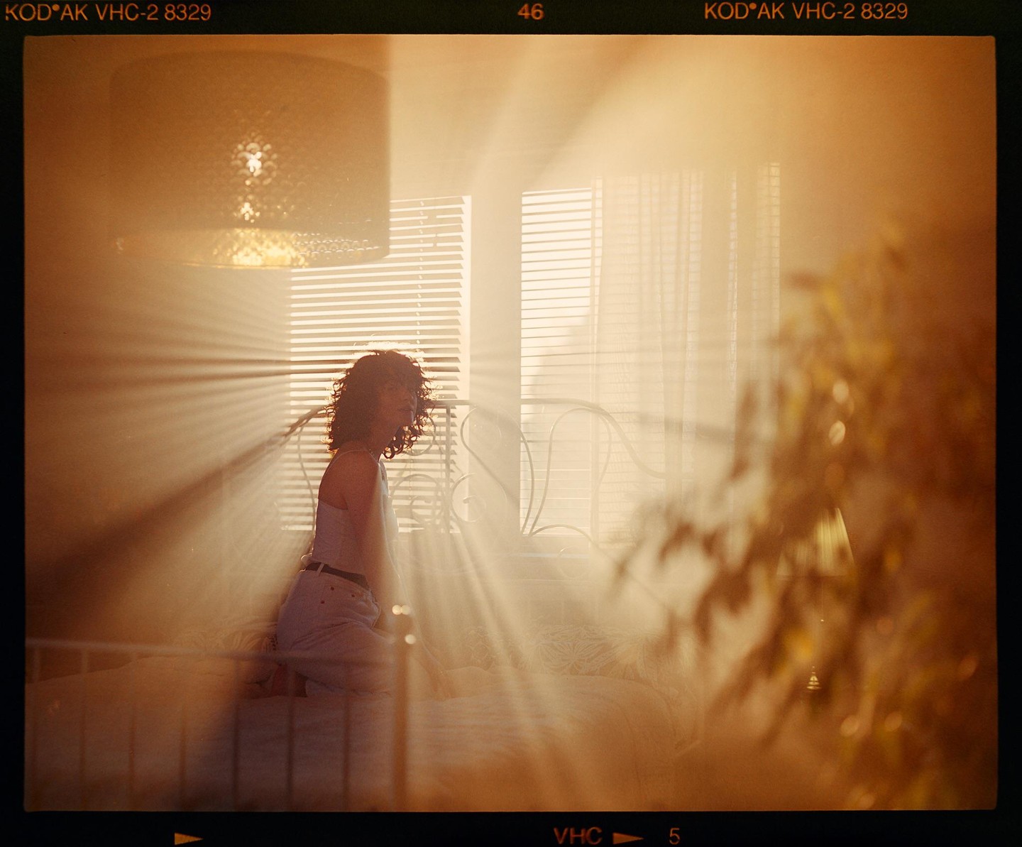 A woman kneels on a bed with light rays streaming through a window.