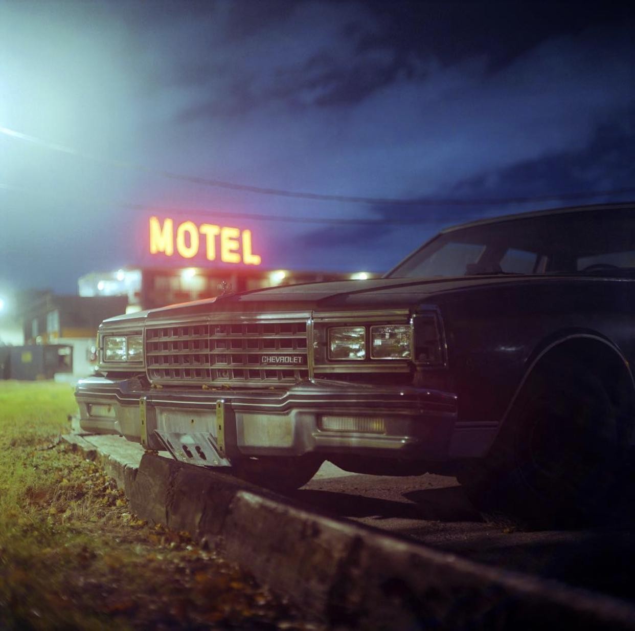 A Chevrolet car is parked in front of a motel sign at night.