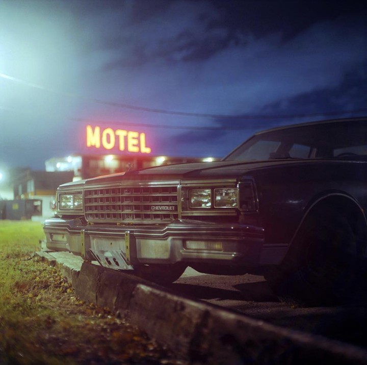 A Chevrolet car is parked in front of a motel sign at night.