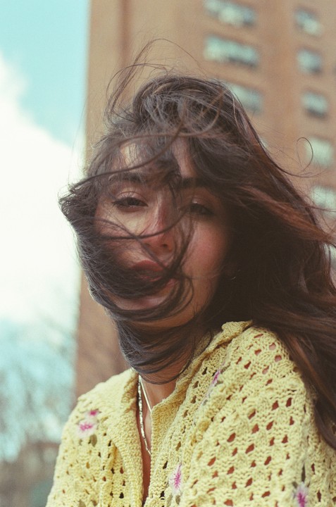 A woman with long, dark hair blowing across her face looks directly at the viewer.
