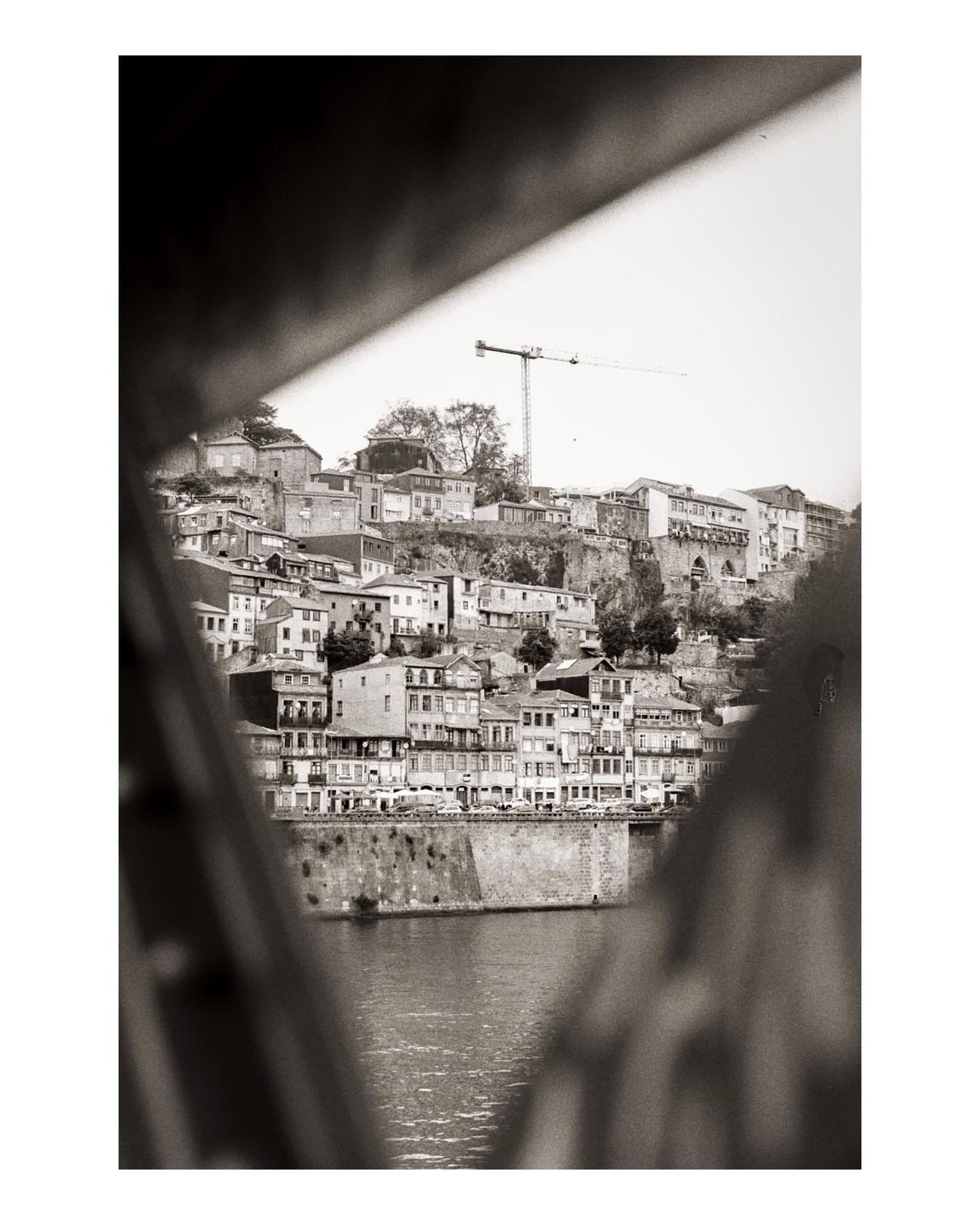 A city built on a hill with a river in front is seen through a triangular opening.