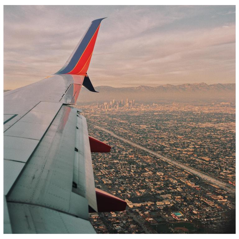 An airplane wing is visible over a sprawling city with mountains in the distance.
