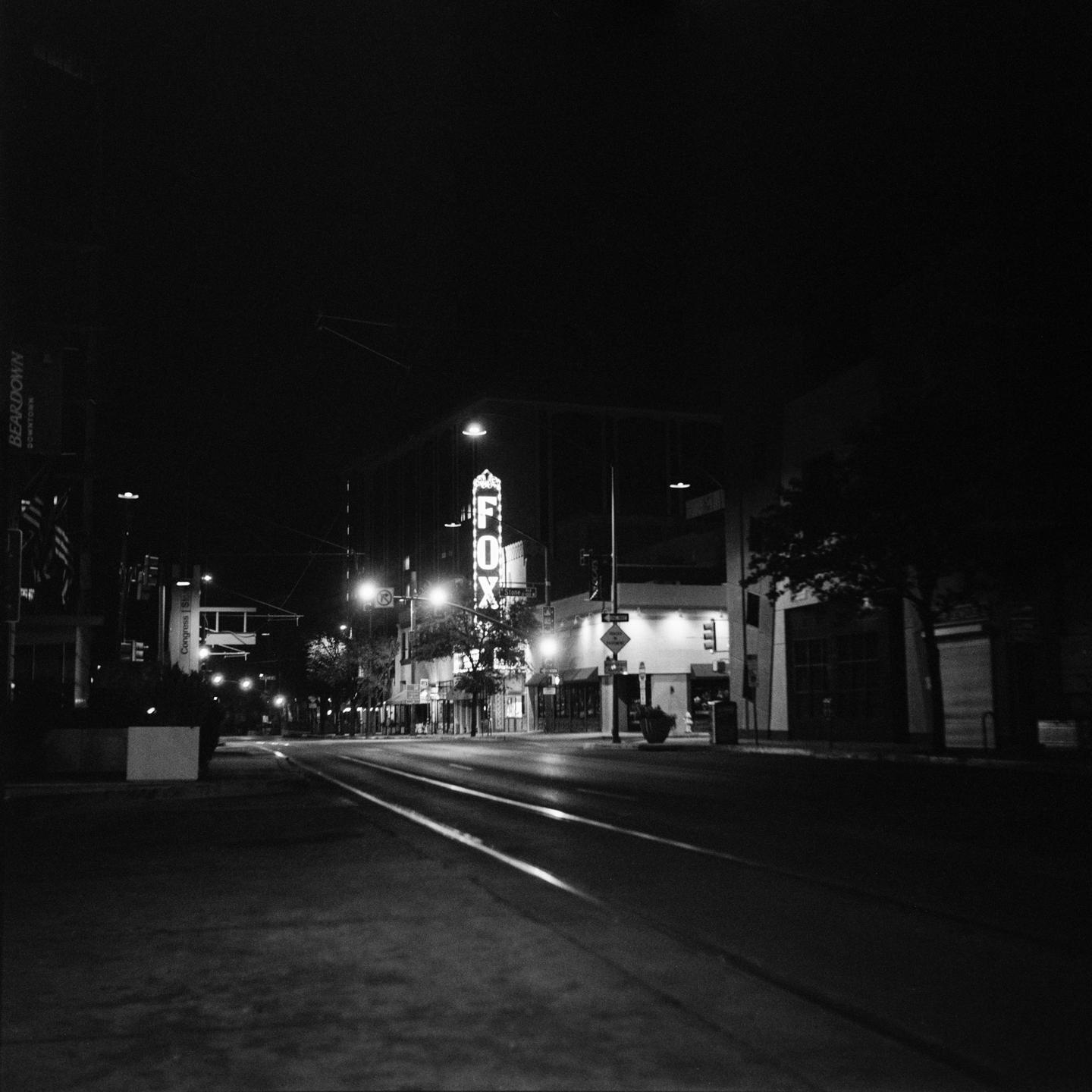 A street at night is illuminated by a neon sign for "FOX" and streetlights.