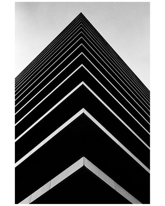 A low-angle view of a modern building shows its sharp corner and horizontal lines against a bright sky.