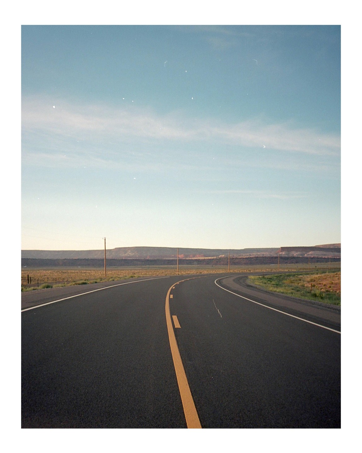A long, empty road curves through a flat, arid landscape under a clear sky.