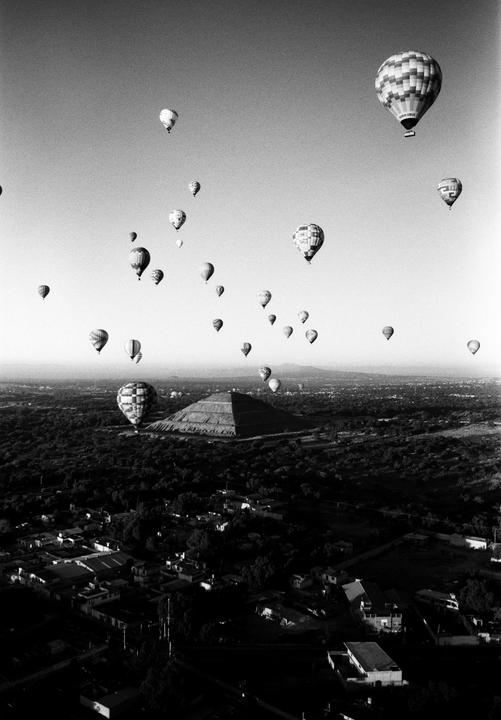 Hot air balloons float above a pyramid and a town in Mexico.