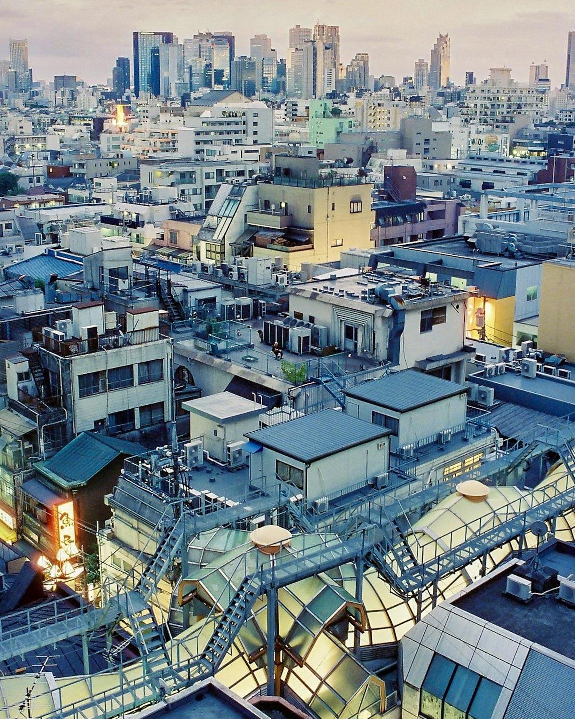 A city with many buildings and a complex rooftop structure is visible from above.