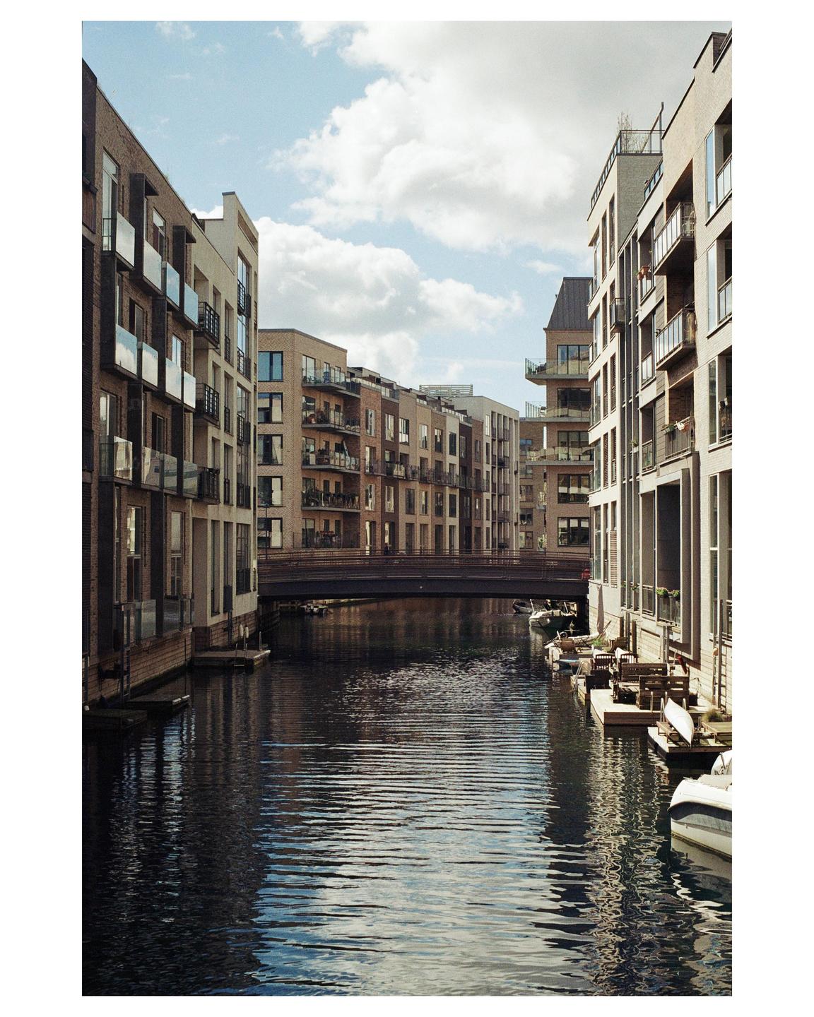 A canal with boats and buildings on both sides is visible under a cloudy sky.