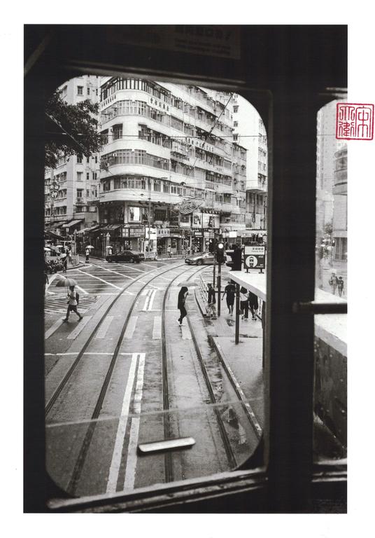 A street with tram tracks and pedestrians is viewed through a tram window.