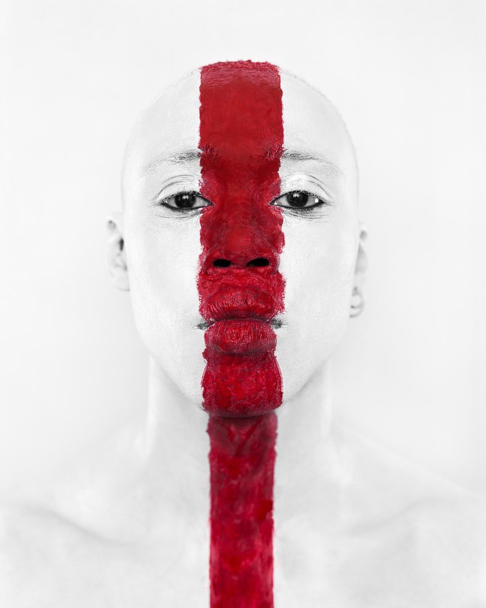 A person with a red stripe painted vertically across their face and body looks directly forward.