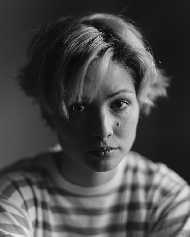 A woman with short hair and a striped shirt looks directly at the viewer.
