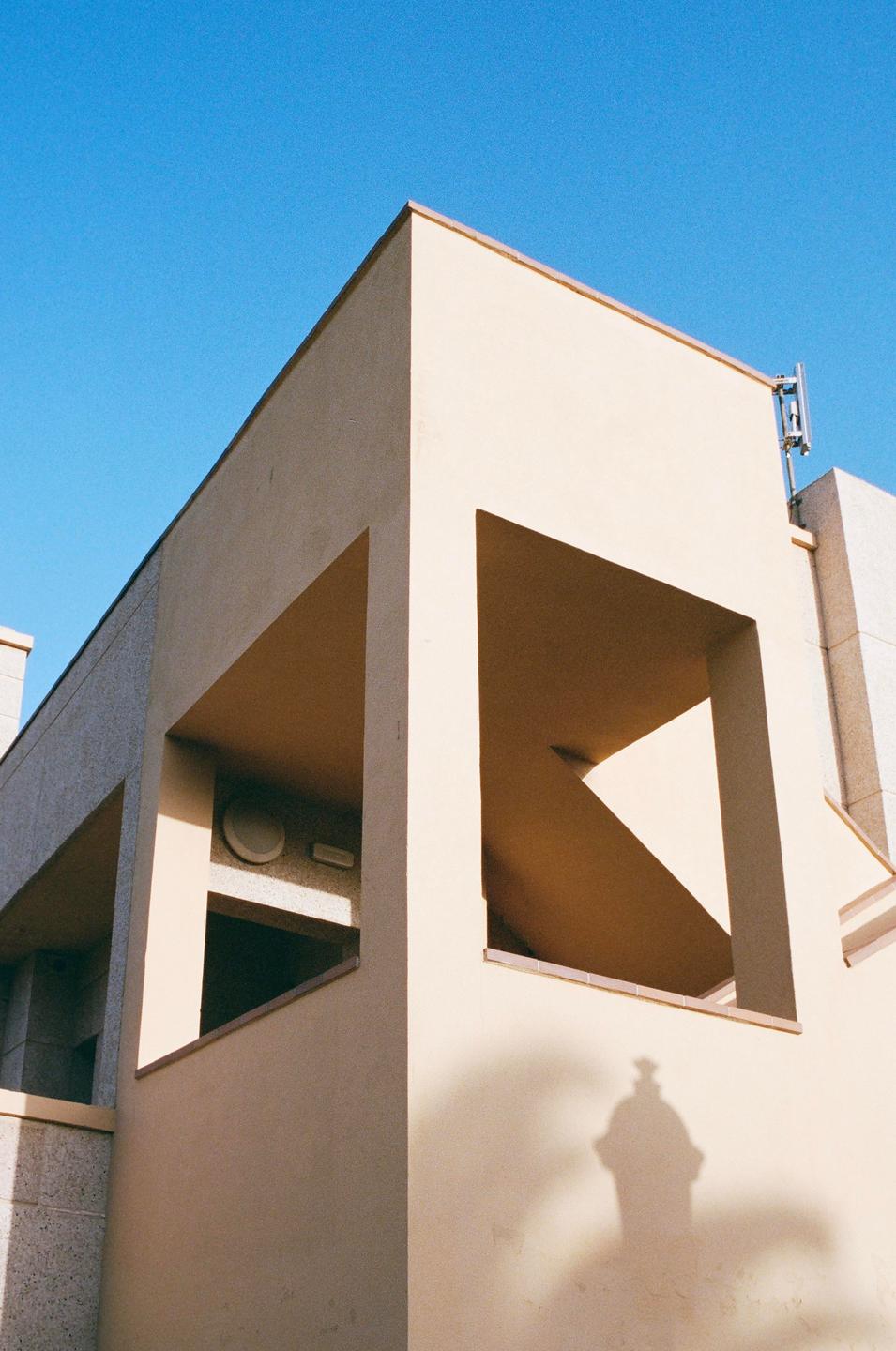 A cream-colored building with geometric cutouts is shown against a clear blue sky.