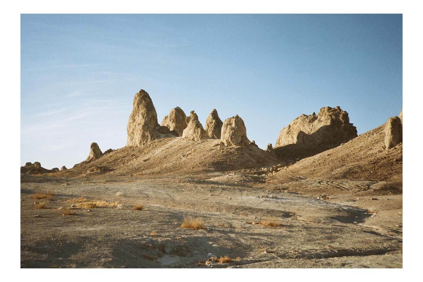 A desert landscape features several tall, rock formations under a clear blue sky.