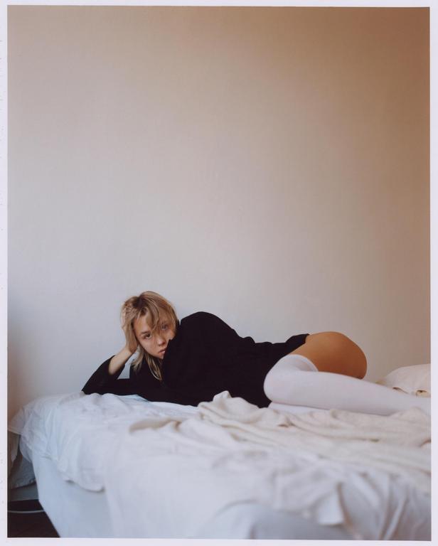 A woman in a black shirt and white thigh-high socks is lying on a bed.