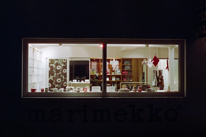 A brightly lit shop window displays various items, including mugs, plates, and textiles, with a person visible inside.