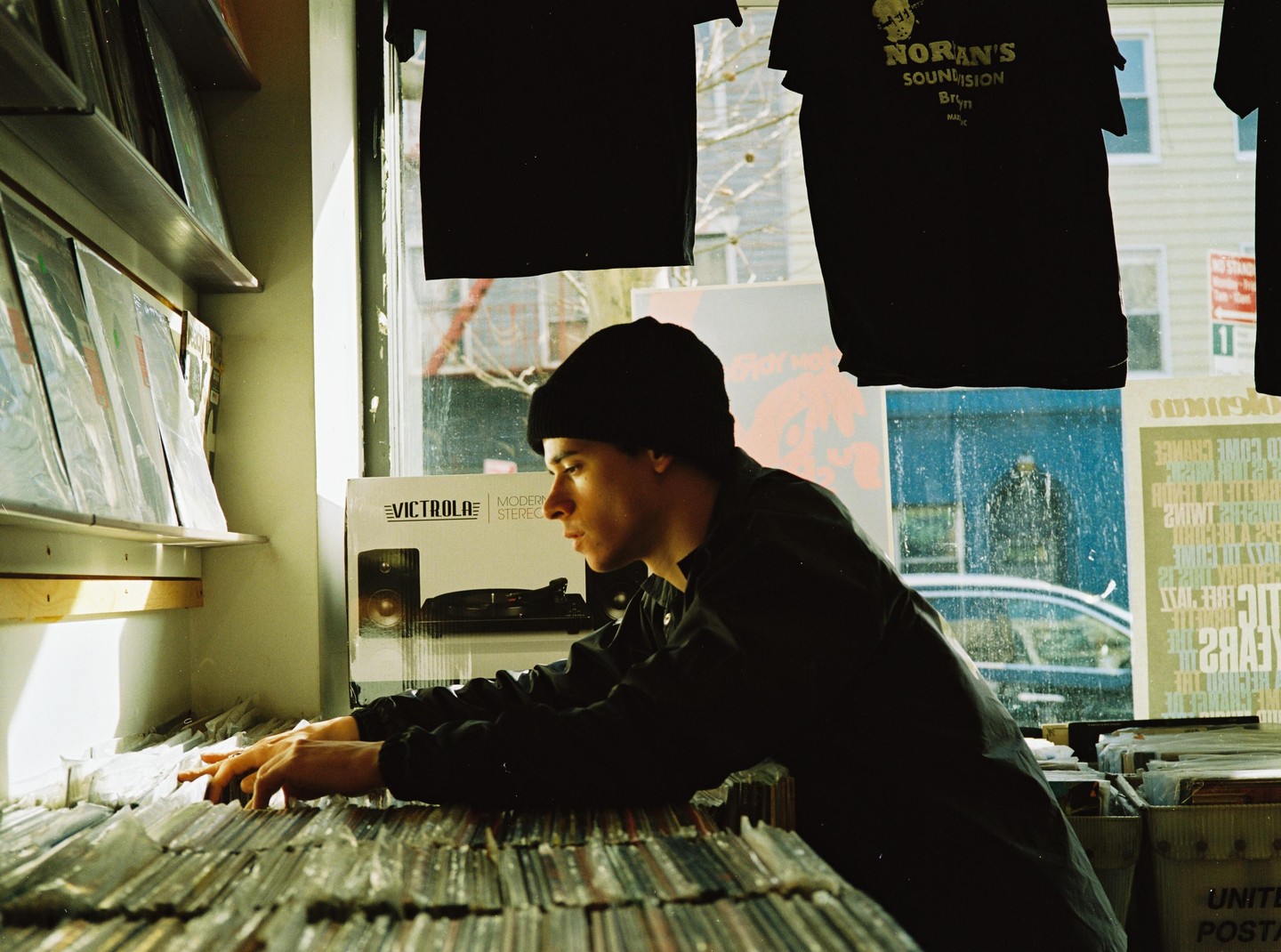 A man in a black beanie and shirt is looking through a bin of vinyl records in a store.