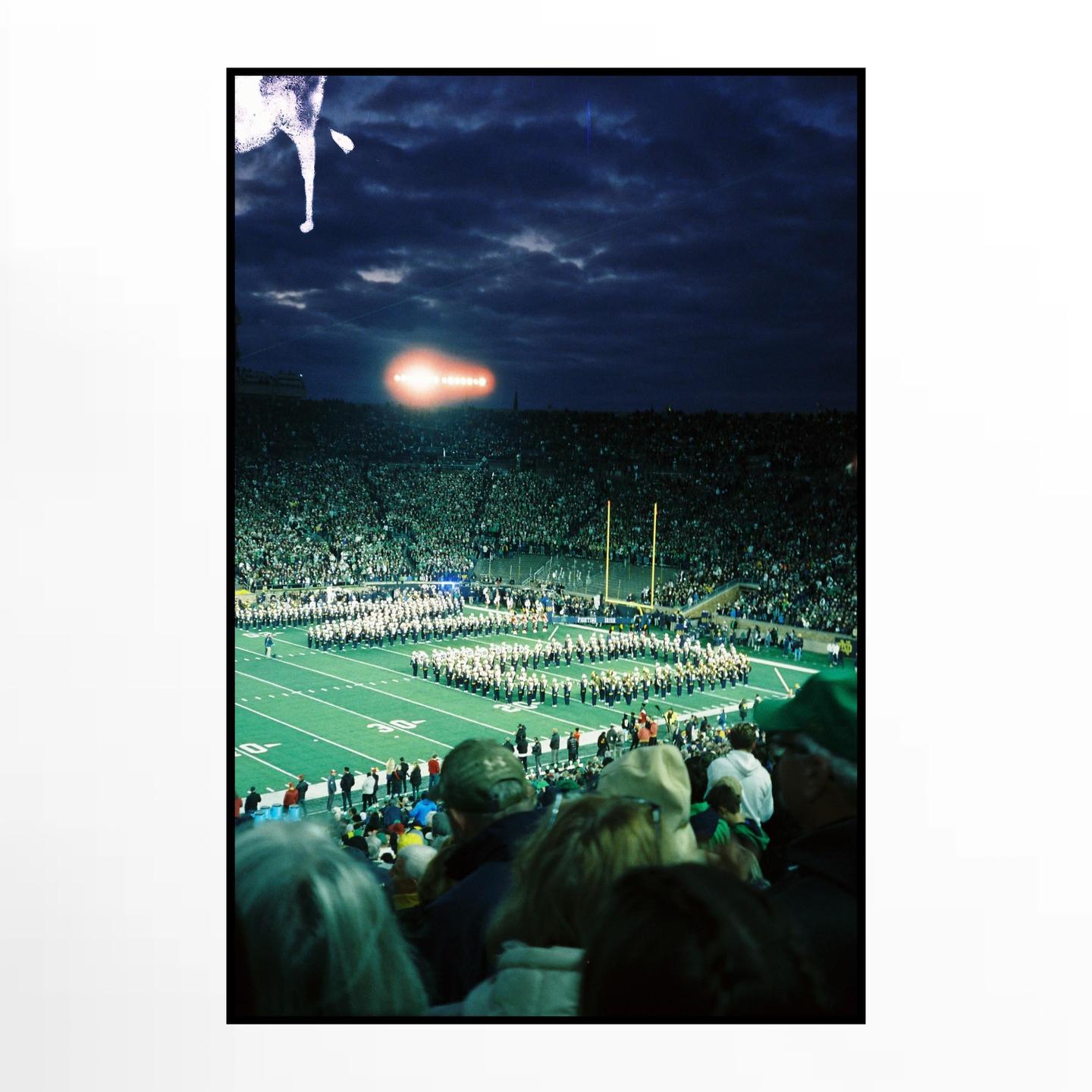 A marching band performs on a football field at night in a stadium filled with spectators.