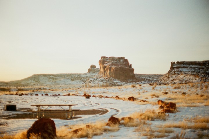 A snowy desert landscape features mesas and picnic tables under a bright sky.